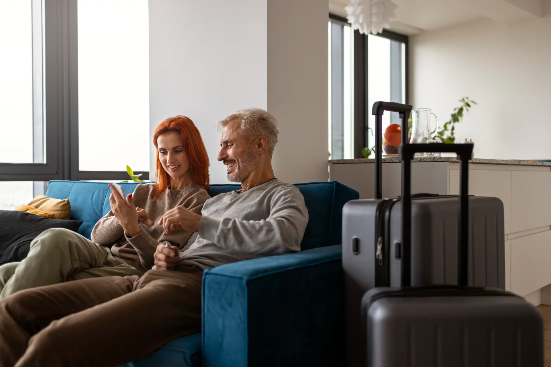 A couple relaxing at home with their suitcases, checking baggage tracking on a phone